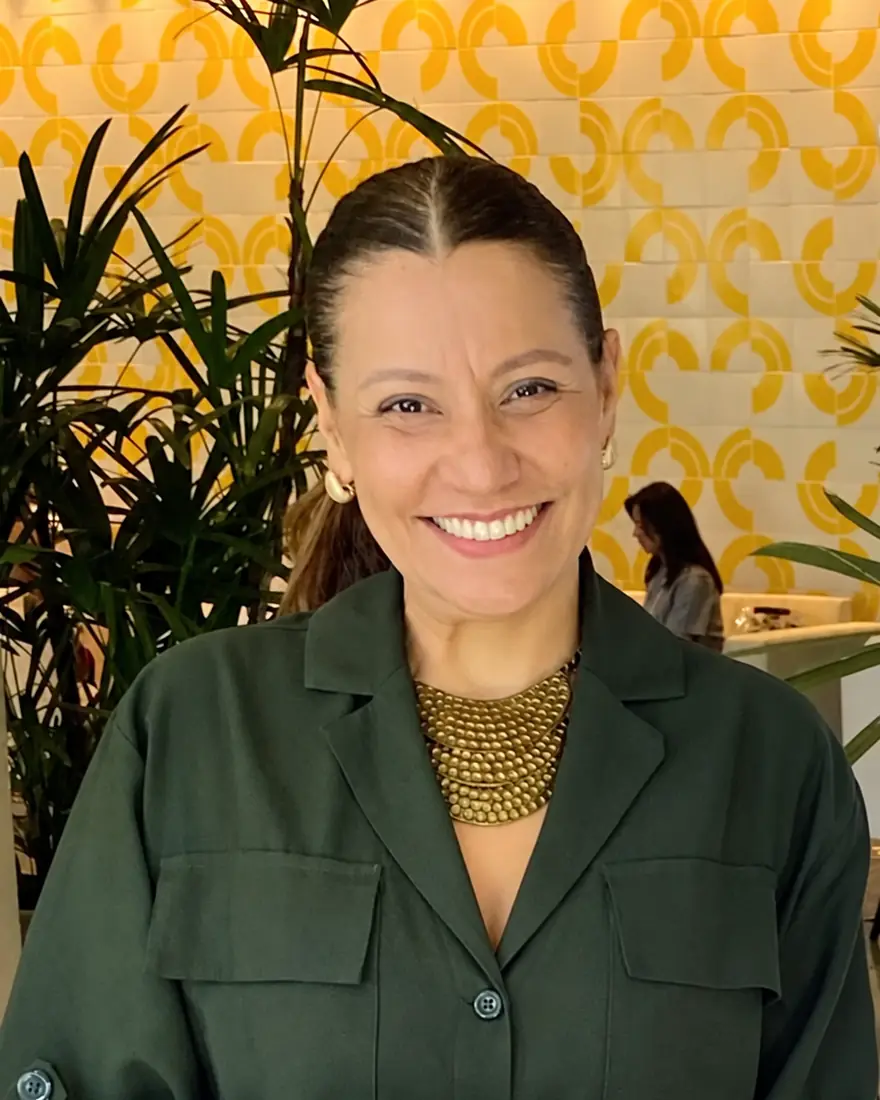 Érika Gadelha sorrindo, de camisa verde e colar dourado